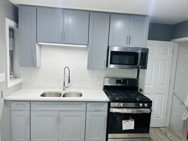 kitchen featuring sink, gray cabinets, appliances with stainless steel finishes, light hardwood / wood-style floors, and light stone counters