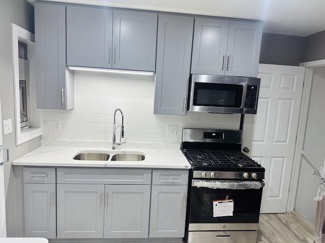 kitchen with stainless steel appliances, light stone counters, light hardwood / wood-style floors, and sink