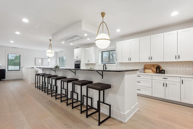 kitchen with white cabinets, stainless steel oven, hanging light fixtures, and light hardwood / wood-style flooring