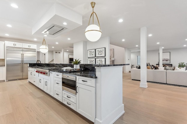 kitchen with appliances with stainless steel finishes, sink, pendant lighting, white cabinets, and light hardwood / wood-style floors