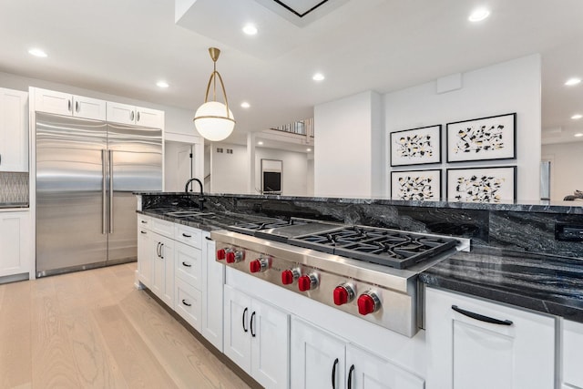 kitchen featuring dark stone countertops, light hardwood / wood-style floors, decorative light fixtures, and appliances with stainless steel finishes