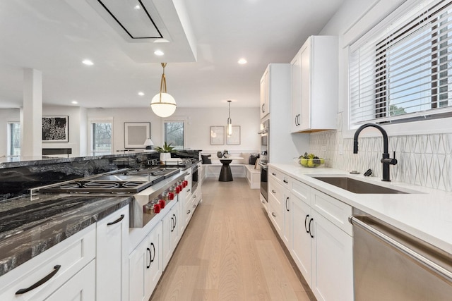 kitchen with white cabinets, sink, light wood-type flooring, decorative light fixtures, and stainless steel appliances