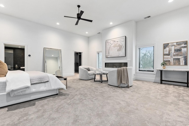 bedroom featuring a high ceiling, a walk in closet, light colored carpet, and ceiling fan