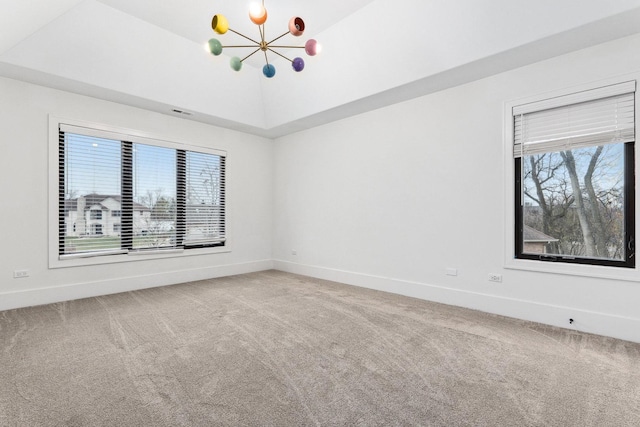 carpeted spare room with a healthy amount of sunlight, vaulted ceiling, and an inviting chandelier