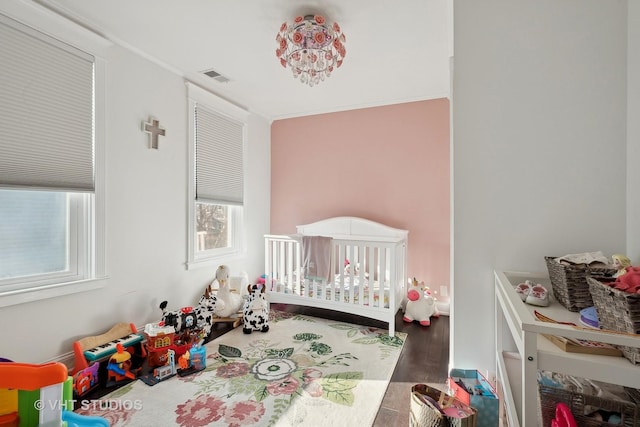 bedroom with wood-type flooring, a crib, and a chandelier