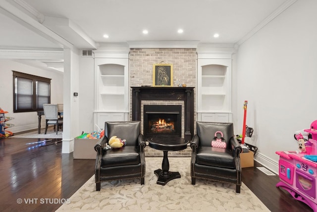 sitting room featuring hardwood / wood-style flooring, crown molding, built in features, and a fireplace