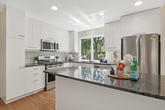 kitchen featuring stainless steel appliances, tasteful backsplash, light wood-type flooring, white cabinets, and dark stone countertops