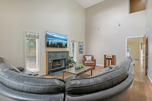 living room featuring a towering ceiling, a tile fireplace, and light hardwood / wood-style flooring