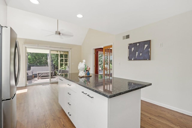 kitchen featuring white cabinetry, lofted ceiling, dark stone countertops, stainless steel refrigerator, and a kitchen island