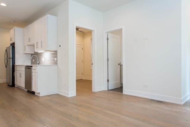 kitchen featuring light wood finished floors, tasteful backsplash, white cabinets, appliances with stainless steel finishes, and light countertops