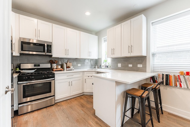 kitchen with a peninsula, appliances with stainless steel finishes, light wood-style flooring, and white cabinets