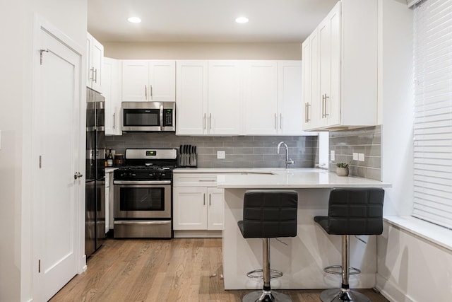 kitchen with white cabinets, a breakfast bar area, a peninsula, stainless steel appliances, and light wood-type flooring