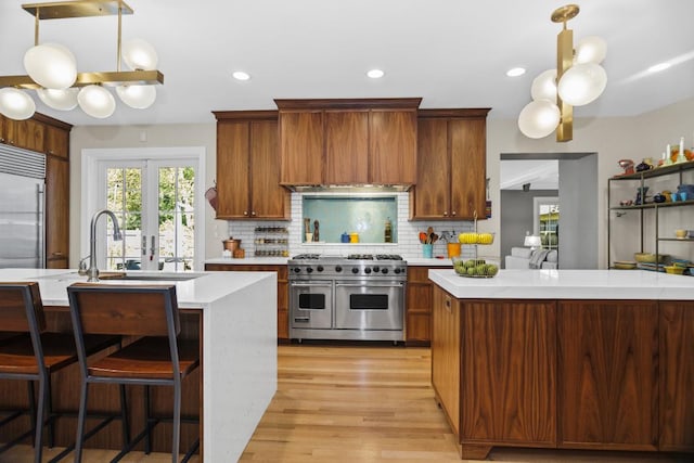 kitchen featuring backsplash, custom exhaust hood, double oven range, hanging light fixtures, and a center island with sink