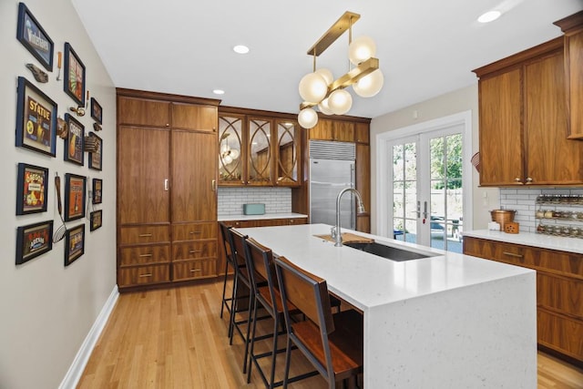 kitchen featuring pendant lighting, built in refrigerator, a kitchen island with sink, and tasteful backsplash