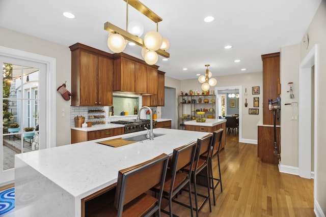 kitchen featuring a breakfast bar, pendant lighting, tasteful backsplash, an island with sink, and light wood-type flooring