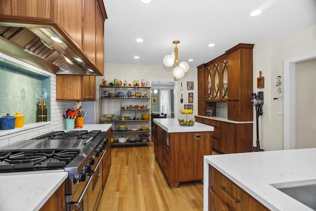 kitchen featuring premium range hood, tasteful backsplash, hanging light fixtures, light wood-type flooring, and stainless steel stove