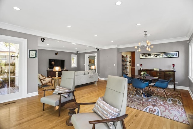 living room with crown molding, a healthy amount of sunlight, a notable chandelier, and light hardwood / wood-style floors