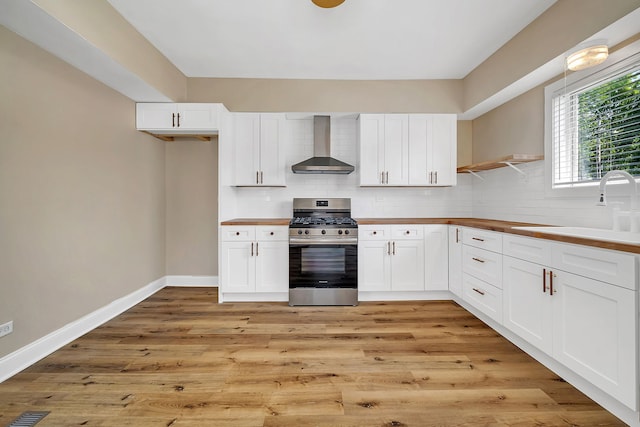 kitchen with white cabinetry, wall chimney exhaust hood, light wood-type flooring, and stainless steel range with gas stovetop