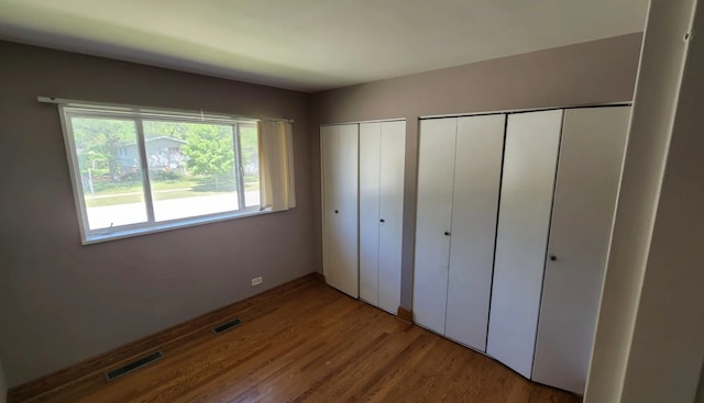 unfurnished bedroom featuring hardwood / wood-style flooring and multiple closets