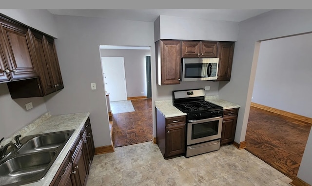 kitchen with dark brown cabinets, light wood-type flooring, stainless steel appliances, and sink