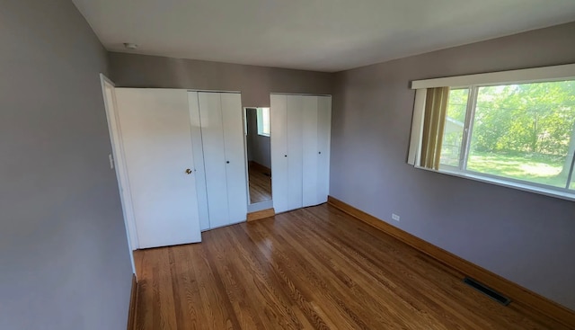 unfurnished bedroom featuring wood-type flooring and multiple closets