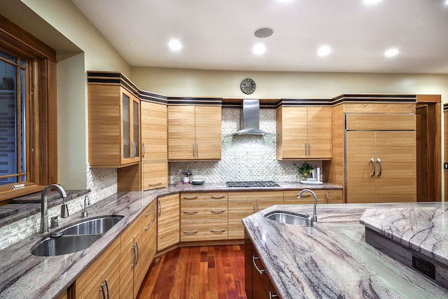 kitchen featuring tasteful backsplash, wall chimney range hood, light stone countertops, and sink