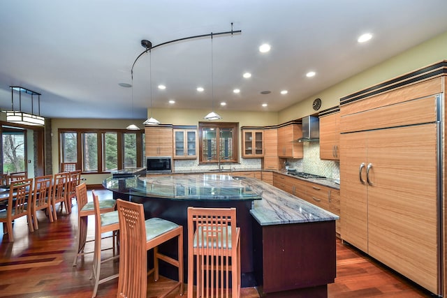 kitchen with decorative light fixtures, dark stone countertops, decorative backsplash, a large island, and wall chimney range hood