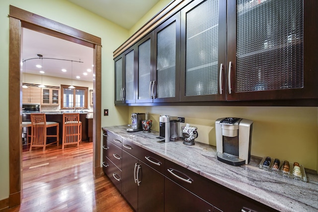 bar featuring dark brown cabinetry, wood-type flooring, light stone countertops, and hanging light fixtures