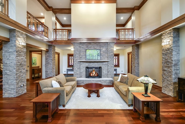 living room with crown molding, a towering ceiling, dark wood-type flooring, and a stone fireplace