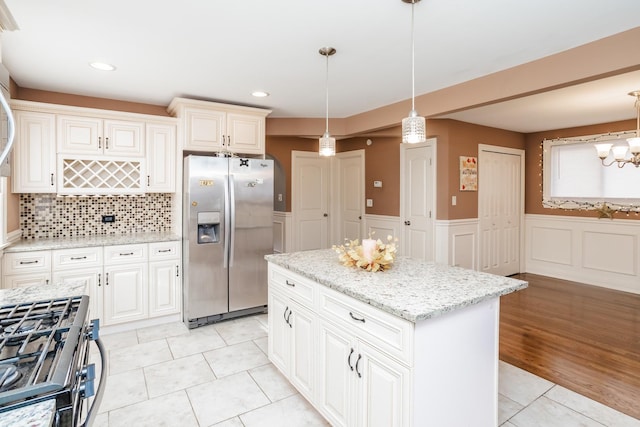 kitchen with backsplash, light tile patterned floors, appliances with stainless steel finishes, decorative light fixtures, and a kitchen island