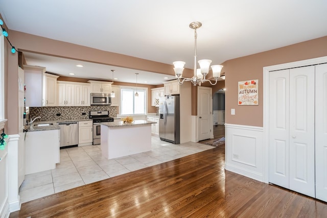 kitchen featuring light stone countertops, a center island, stainless steel appliances, a notable chandelier, and pendant lighting