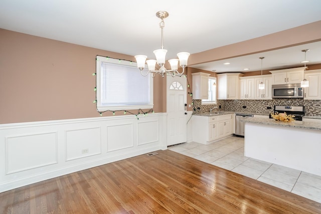 kitchen featuring sink, stainless steel appliances, an inviting chandelier, light stone counters, and decorative light fixtures