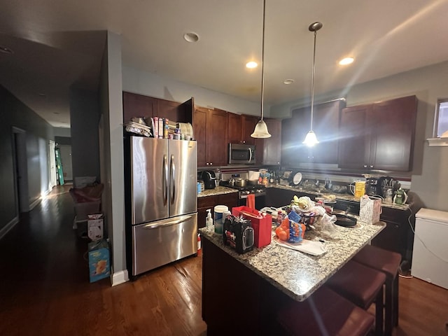 kitchen with light stone counters, stainless steel appliances, decorative light fixtures, dark hardwood / wood-style floors, and a kitchen island