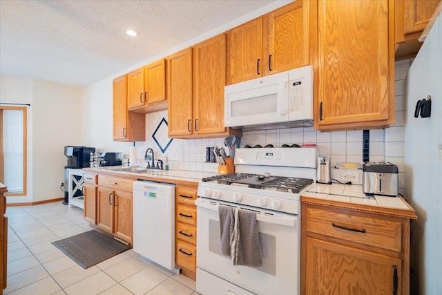 kitchen featuring white appliances, a textured ceiling, light tile patterned flooring, sink, and backsplash