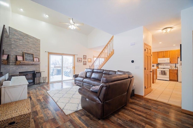 living room with a large fireplace, ceiling fan, light hardwood / wood-style floors, and a high ceiling