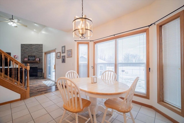 dining room with a stone fireplace, vaulted ceiling, light tile patterned flooring, and ceiling fan with notable chandelier