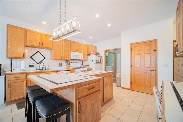 kitchen featuring white appliances, a breakfast bar area, a center island, tile countertops, and sink