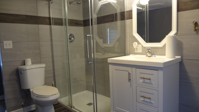 bathroom with vanity, toilet, a shower with shower door, and tile walls