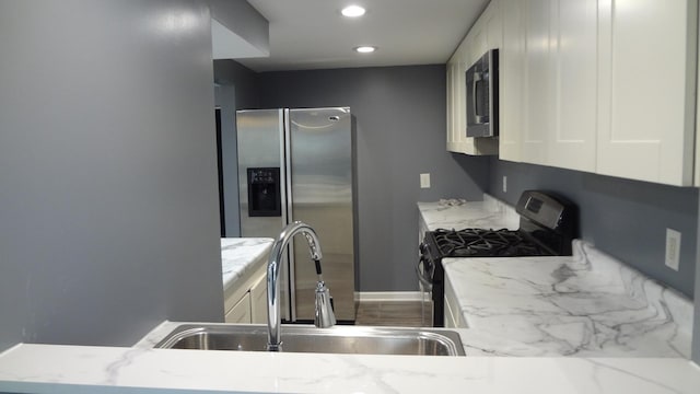 kitchen with white cabinets, stainless steel appliances, light stone countertops, and sink