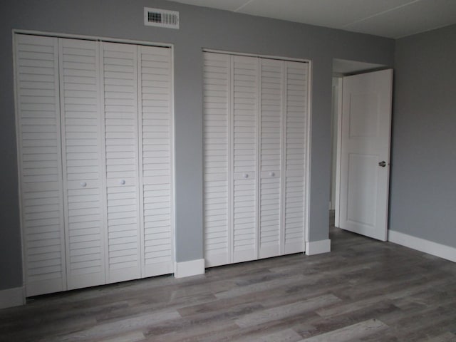 unfurnished bedroom with wood-type flooring and two closets