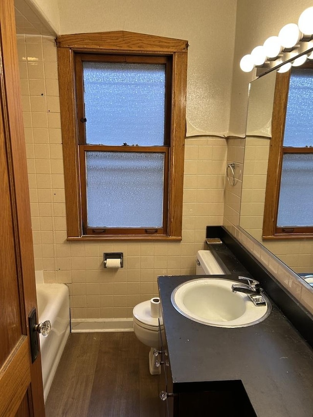 bathroom with a tub, hardwood / wood-style floors, tile walls, and toilet