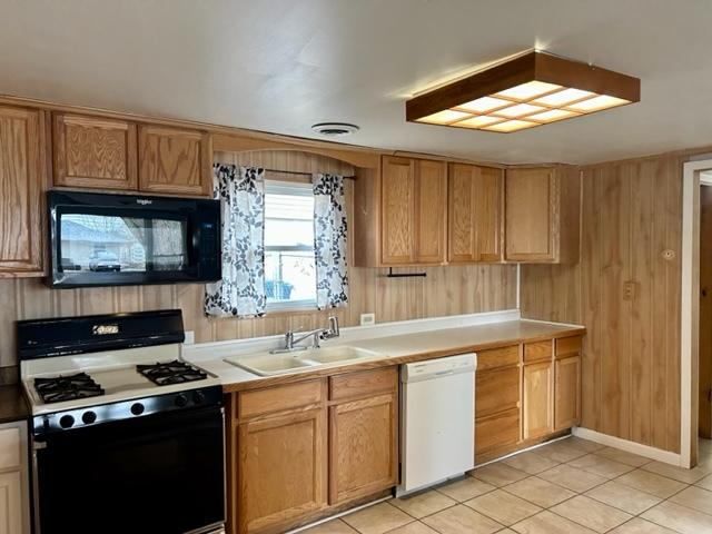 kitchen with light tile patterned flooring, sink, wooden walls, and black appliances