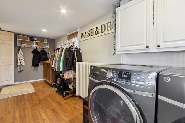 laundry room featuring light wood-type flooring, radiator heating unit, washing machine and dryer, and cabinets