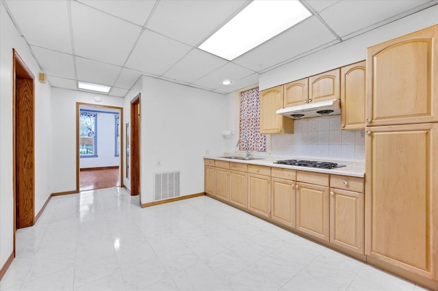 kitchen featuring a paneled ceiling, light brown cabinets, gas stovetop, and tasteful backsplash