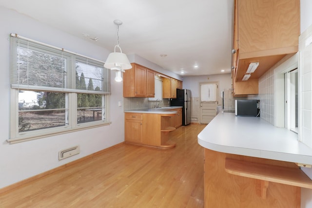 kitchen featuring decorative light fixtures, light hardwood / wood-style flooring, stainless steel fridge, kitchen peninsula, and decorative backsplash