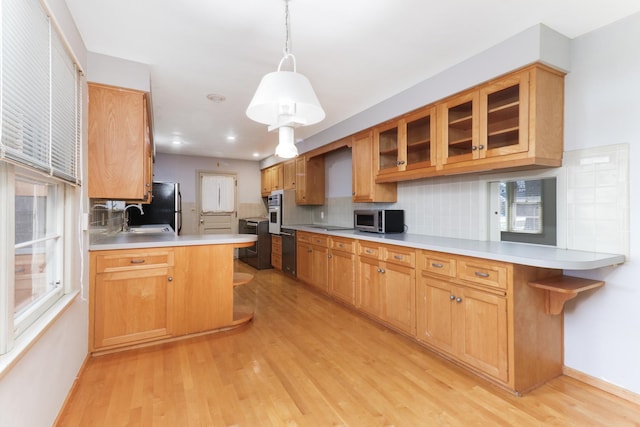 kitchen with a kitchen bar, sink, hanging light fixtures, kitchen peninsula, and light hardwood / wood-style floors