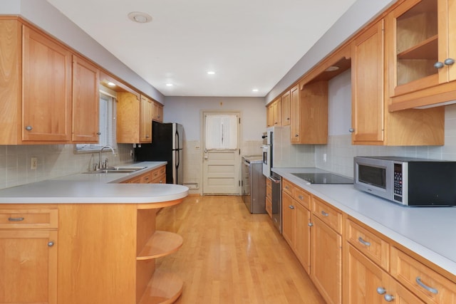 kitchen with appliances with stainless steel finishes, sink, decorative backsplash, kitchen peninsula, and light hardwood / wood-style flooring