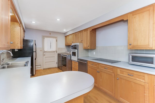 kitchen with sink, appliances with stainless steel finishes, washing machine and dryer, decorative backsplash, and light wood-type flooring