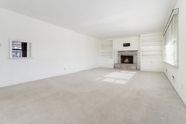 unfurnished living room featuring light carpet, a stone fireplace, and built in shelves