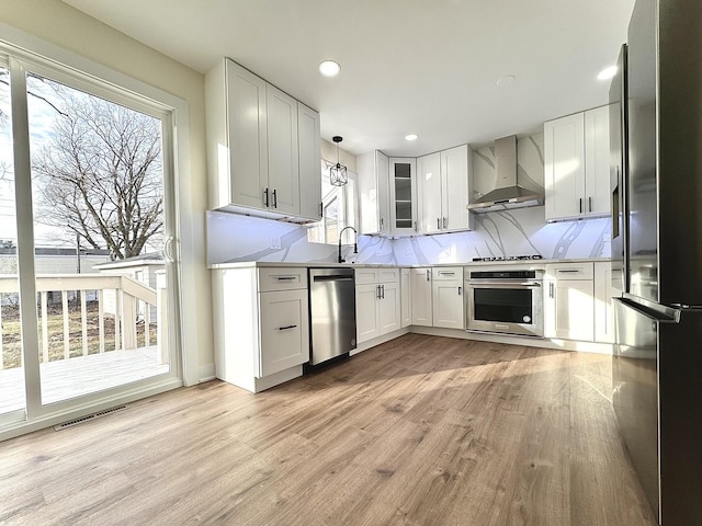 kitchen featuring white cabinets, wall chimney range hood, stainless steel appliances, and hanging light fixtures